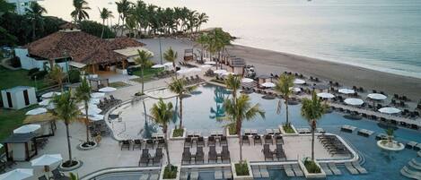 A resort with a swimming pool, beach, and mountains in the background.
