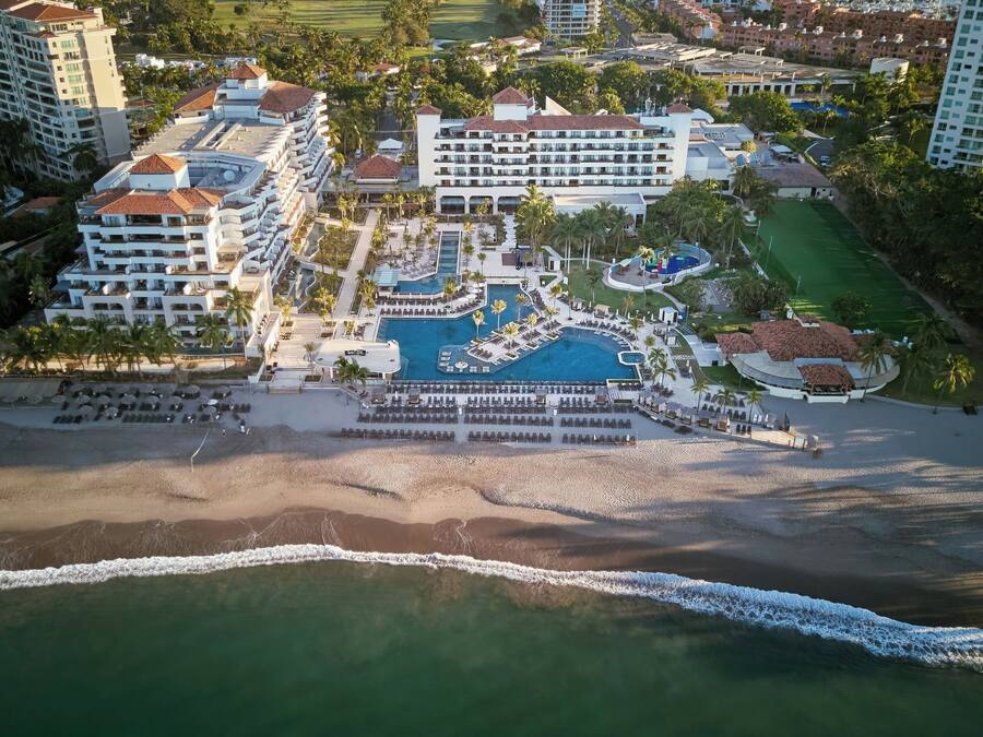 Ein Luftbild eines Resorts mit mehreren Gebäuden, einem großen Poolbereich und einem Strand.