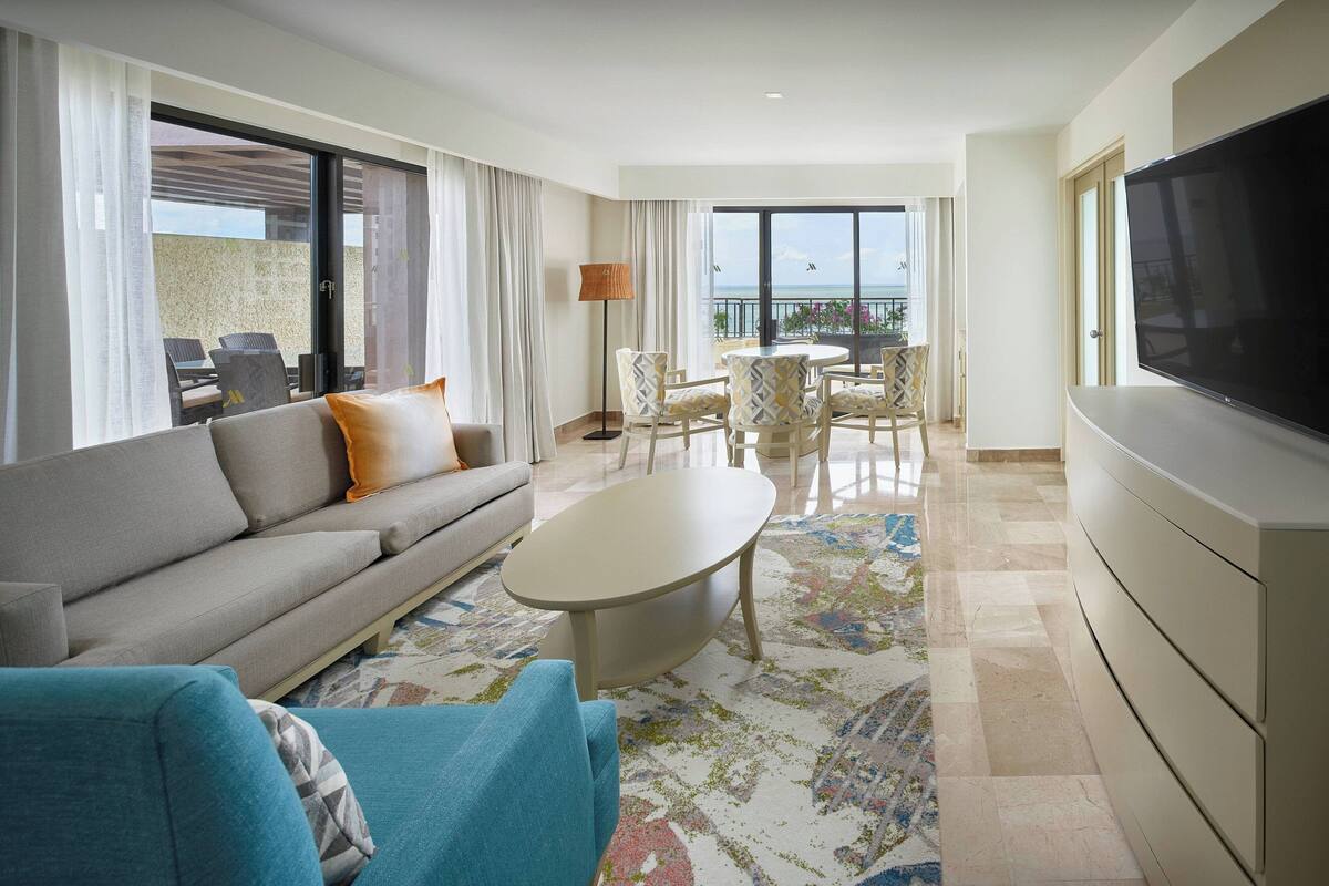 A modern hotel room with a sofa, armchair, coffee table, and a TV.