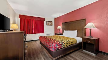 Habitación de hotel con cama, dos mesitas de noche con lámparas, televisor, cortina roja y cabecero de madera.