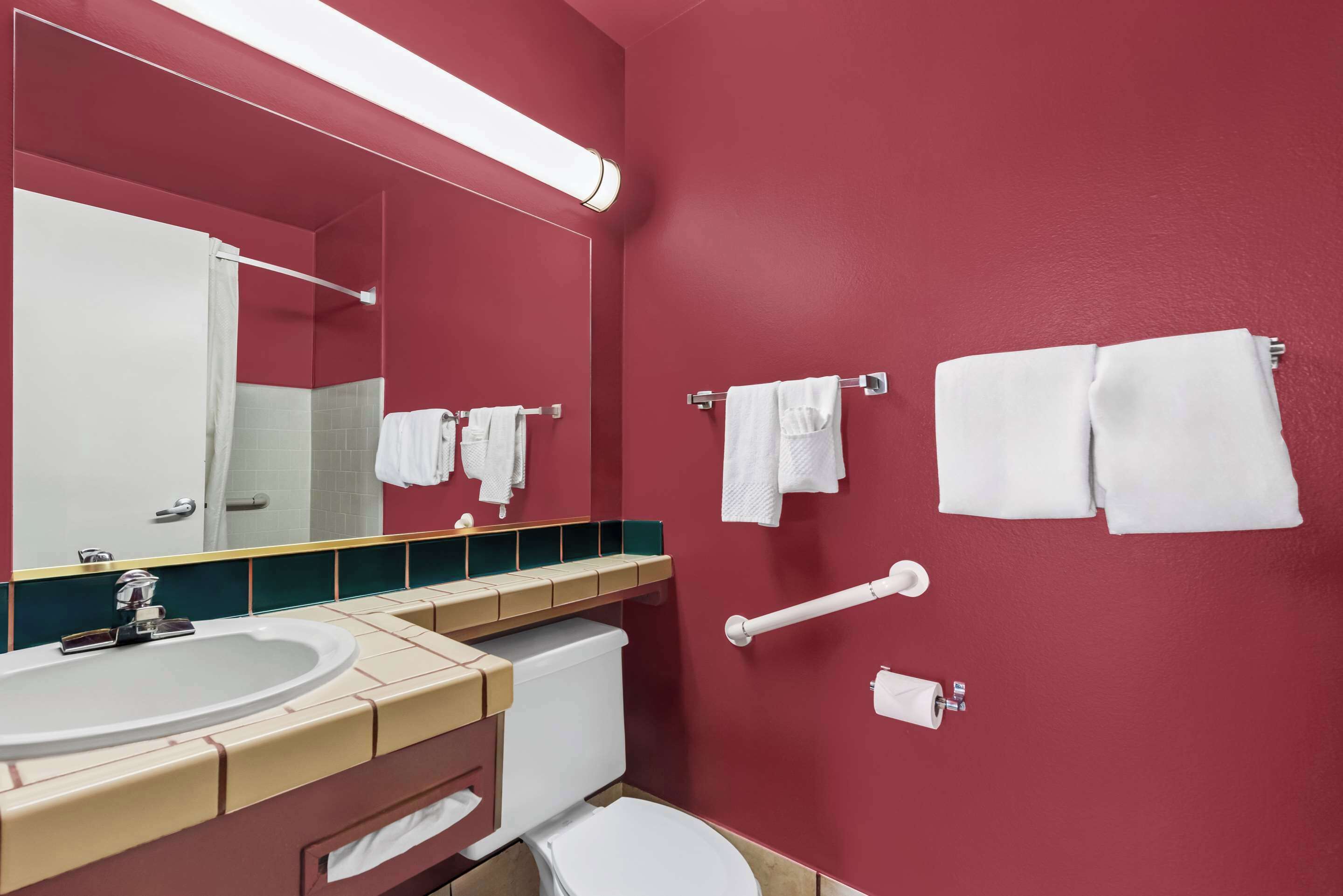 Un baño con lavamanos, espejo, inodoro y perchero para toallas.