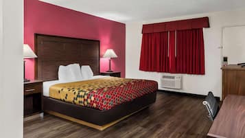 A hotel room with a bed, bedside tables, a desk, and a window with red curtains.