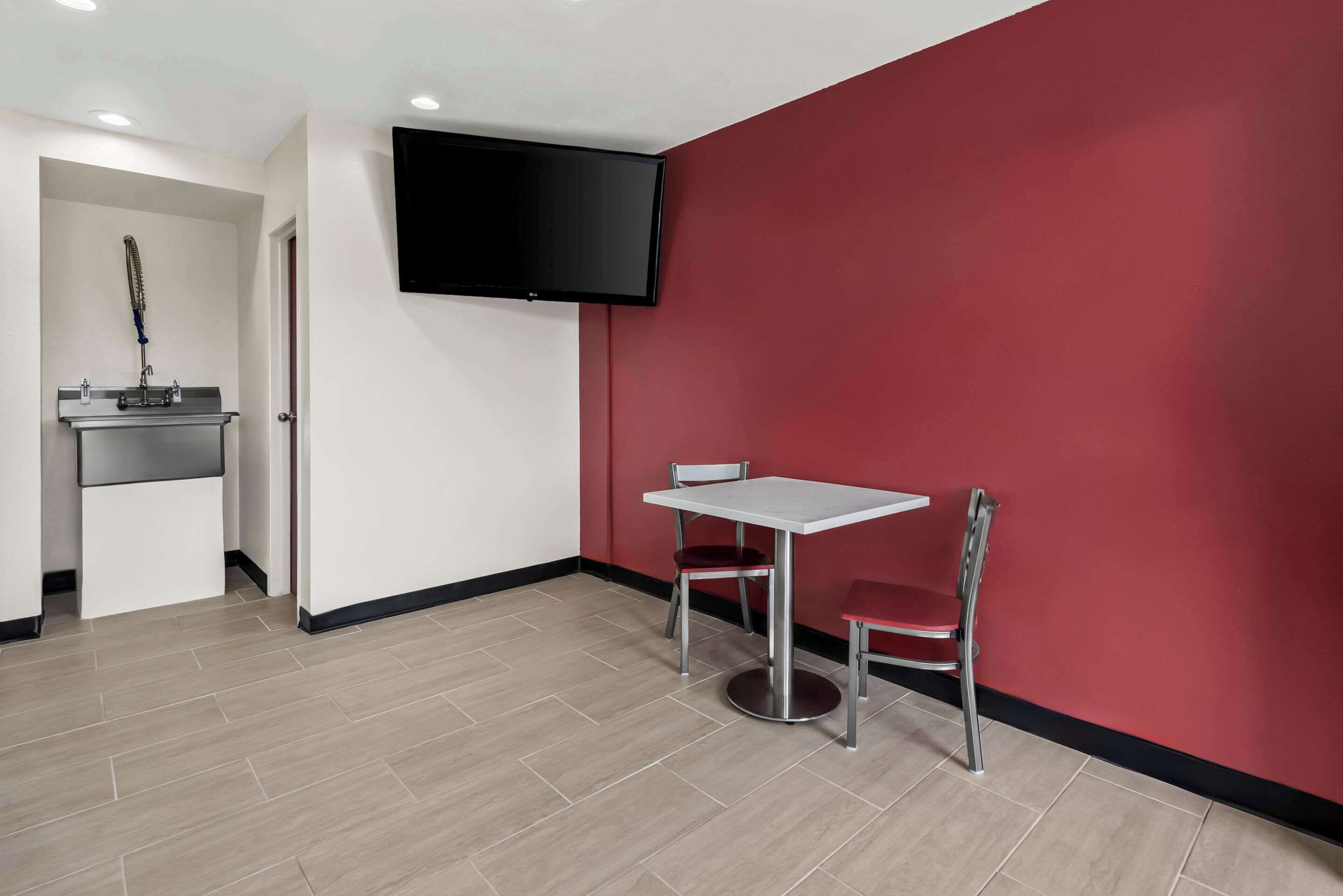 Une pièce avec une table blanche et deux chaises, un téléviseur à écran plat fixé au mur et un espace douche équipé d’un pommeau de douche à main.