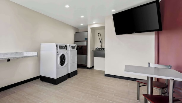 Une cuisine moderne équipée d’un lave-linge et d’un sèche-linge intégrés, d’un téléviseur à écran plat fixé au mur et d’un petit coin repas avec une table et des chaises.