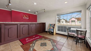 Un espace d’accueil avec un mur rouge, une enseigne EconoLodge, un tableau d’affichage et une vue sur des maisons à travers une grande fenêtre.