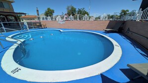 Une piscine ronde avec une bordure bleue, une clôture en métal et un mur de briques en arrière-plan.