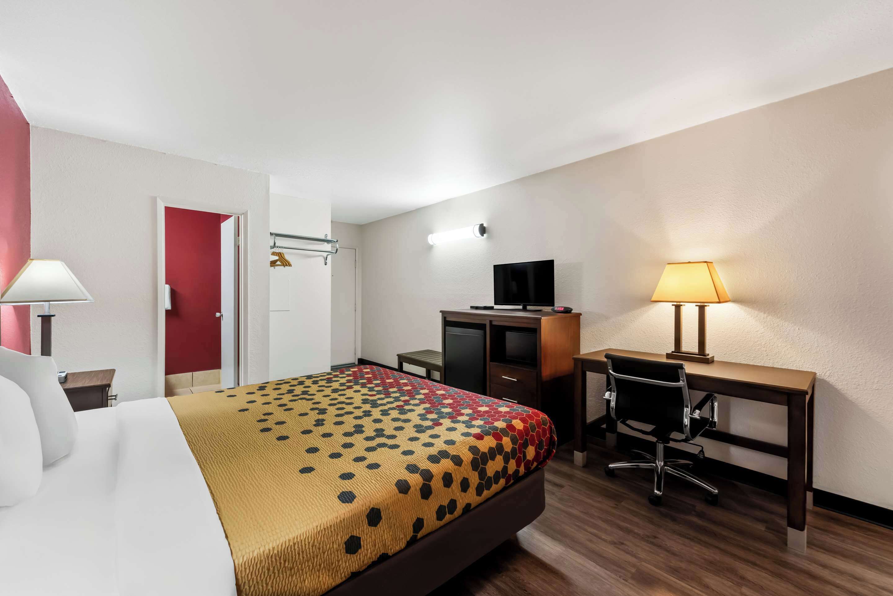 A hotel room with a bed, a desk, a chair, a TV, and a lamp.