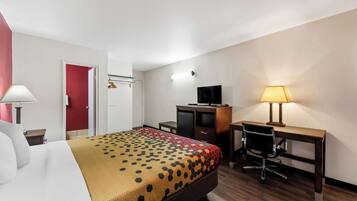 A hotel room with a bed, a desk, a chair, a TV, and a lamp.