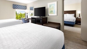 A hotel room with two beds, a TV, a desk, and a view of the outdoors.