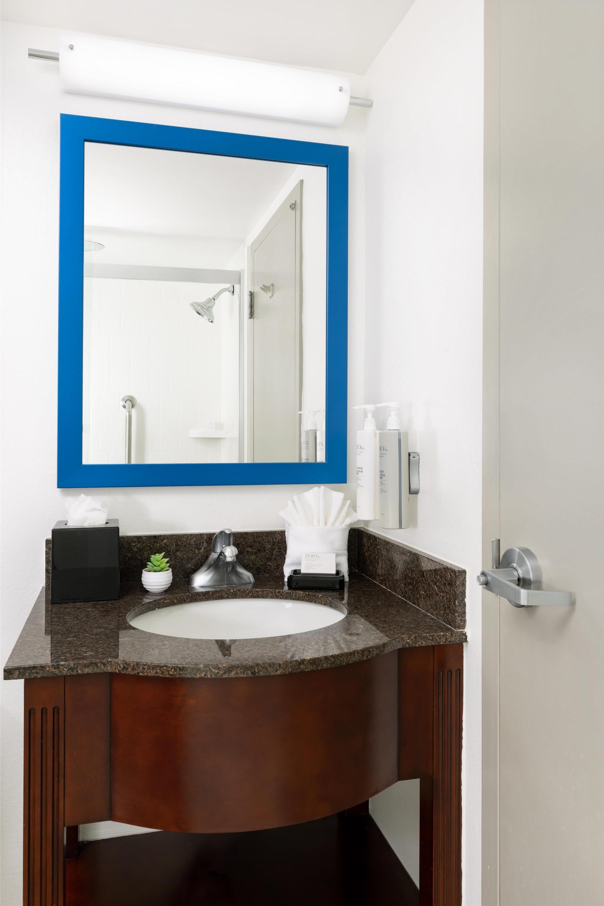 A bathroom with a white sink, dark wood vanity, a blue-framed mirror, and a white towel dispenser.