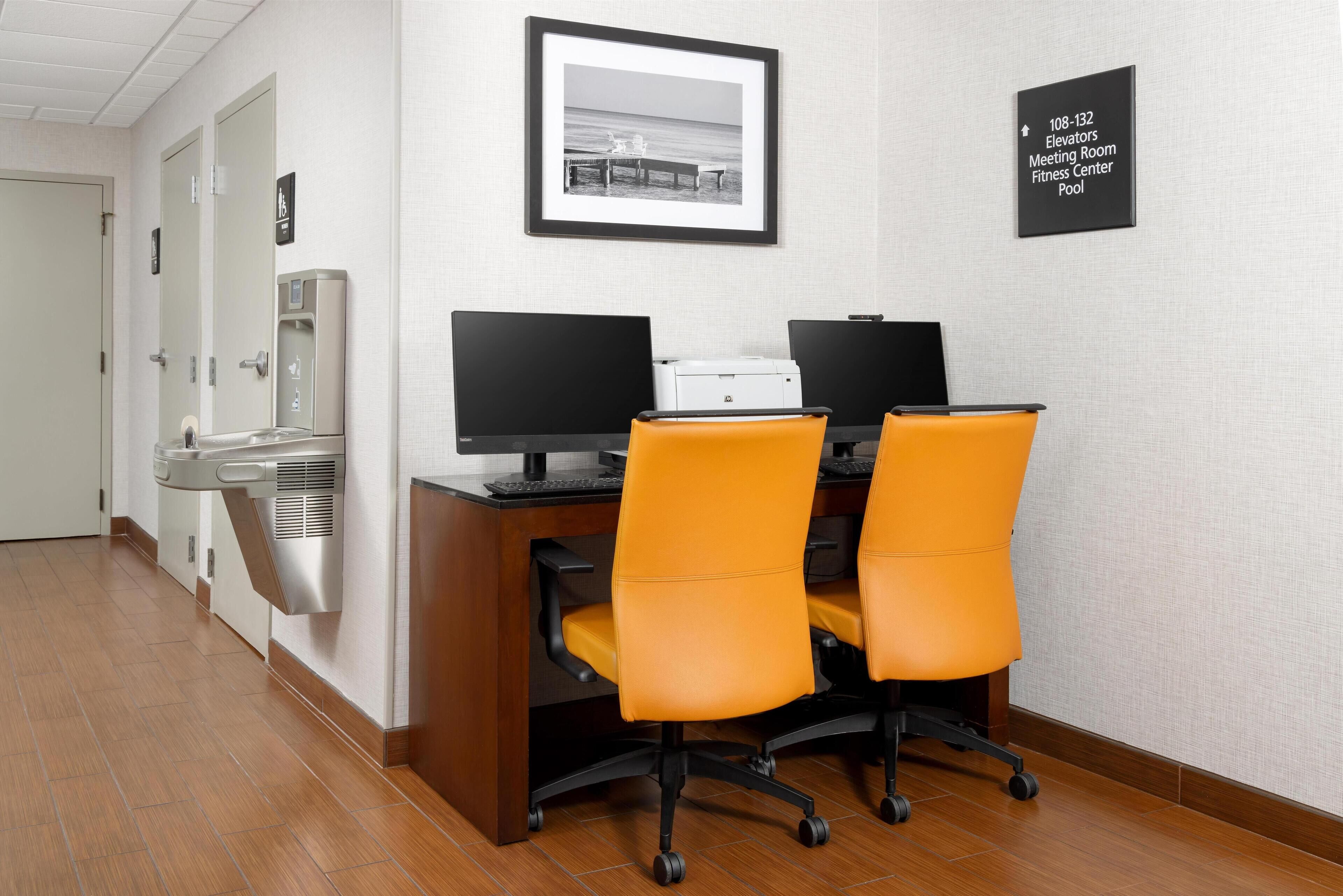 A hotel office with two desks, two chairs, a printer, and a water dispenser.