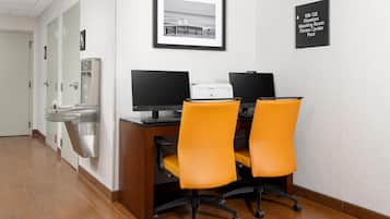A hotel office with two desks, two chairs, a printer, and a water dispenser.