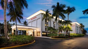 A hotel with a modern facade, palm trees, and a well-lit entrance.