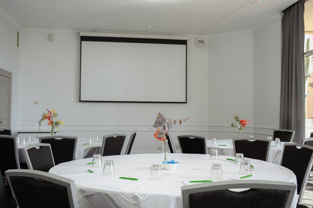 A conference room with a large screen, round tables, and chairs.