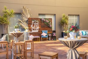 Un patio al aire libre con mobiliario de madera, una pared decorativa con un cartel que dice 'Live Take a Selfie' y varias plantas en macetas.