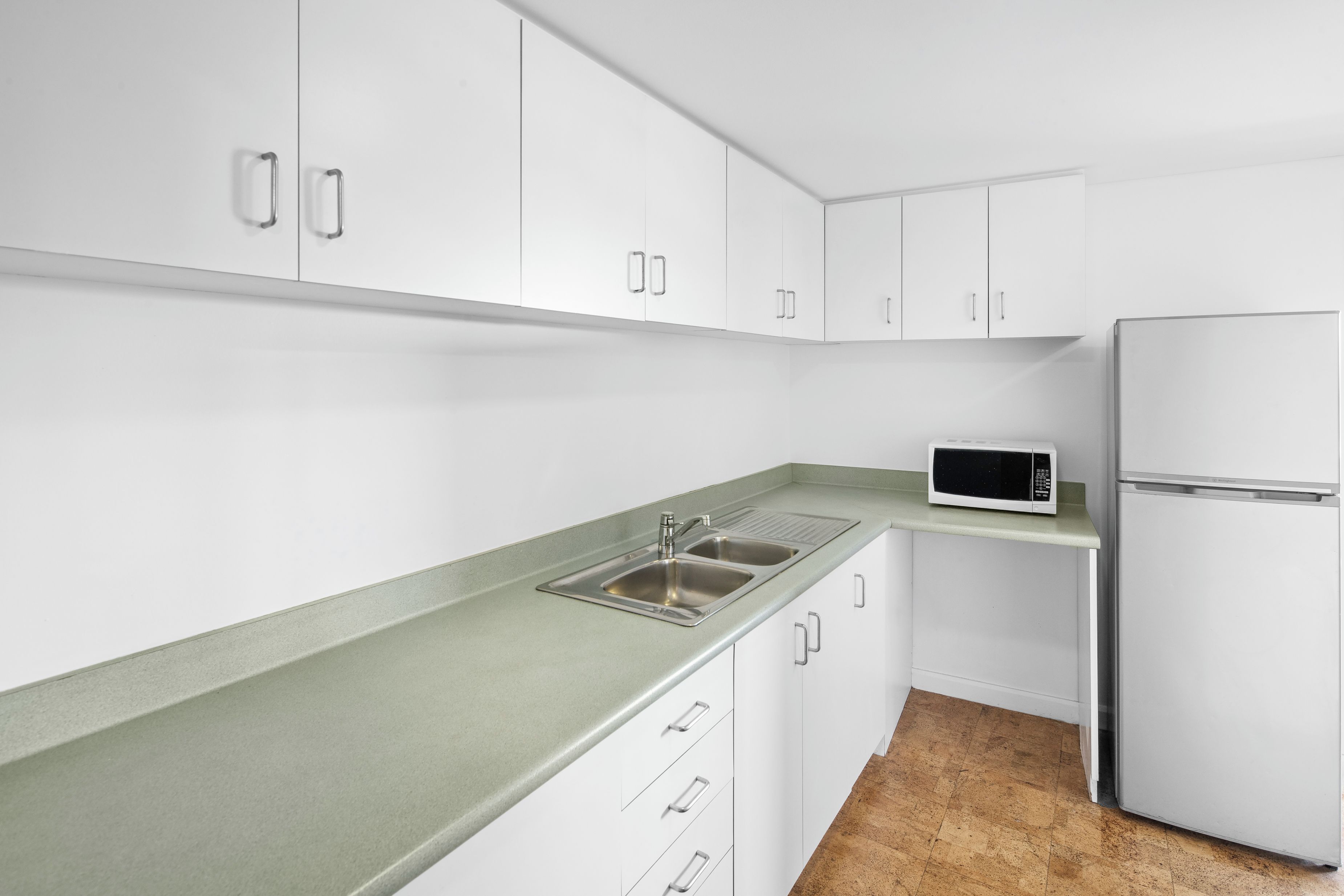 A kitchen with white cabinets, a stainless steel sink, a microwave, and a refrigerator.