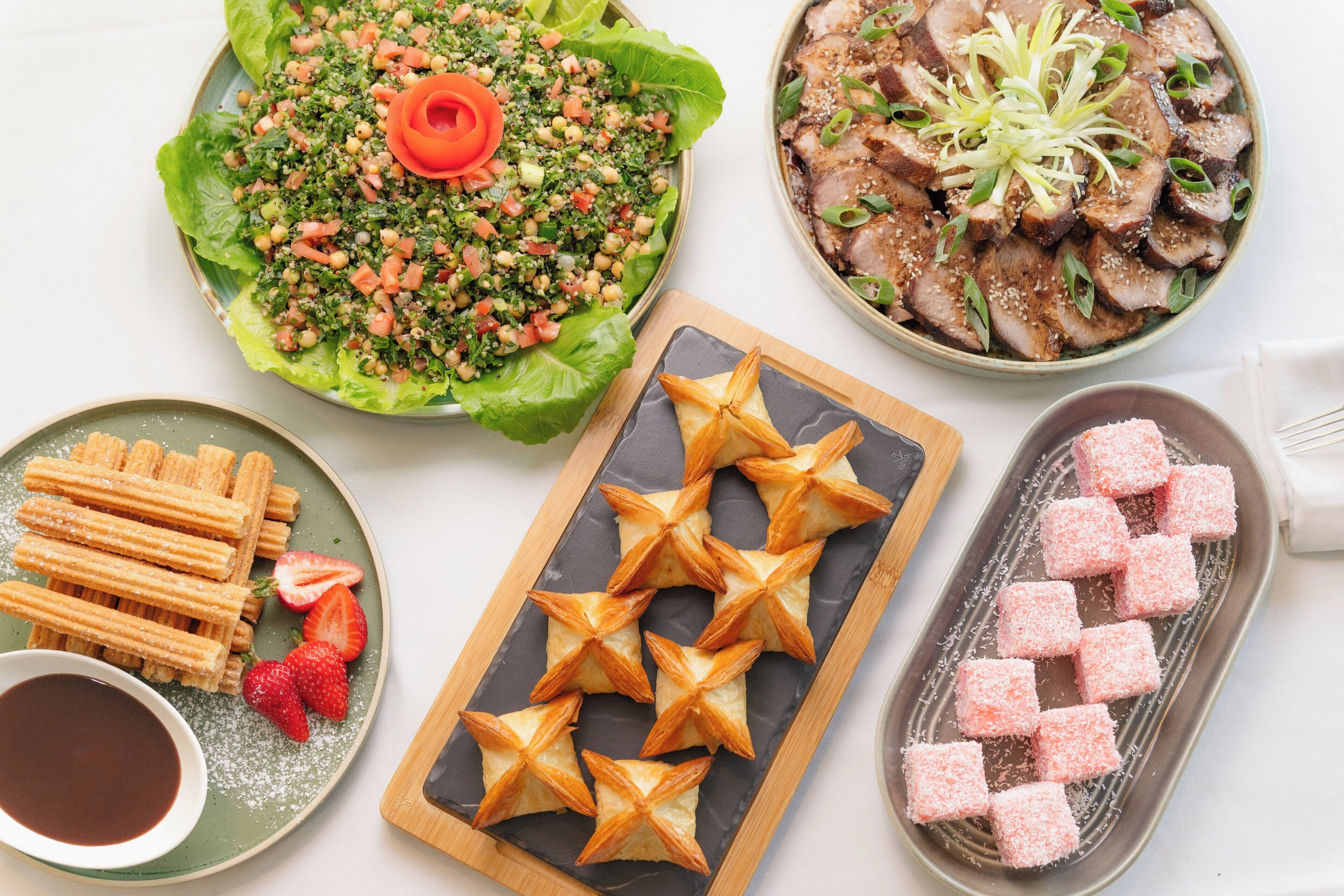 A variety of dishes including a salad, meat, churros, and pastries.