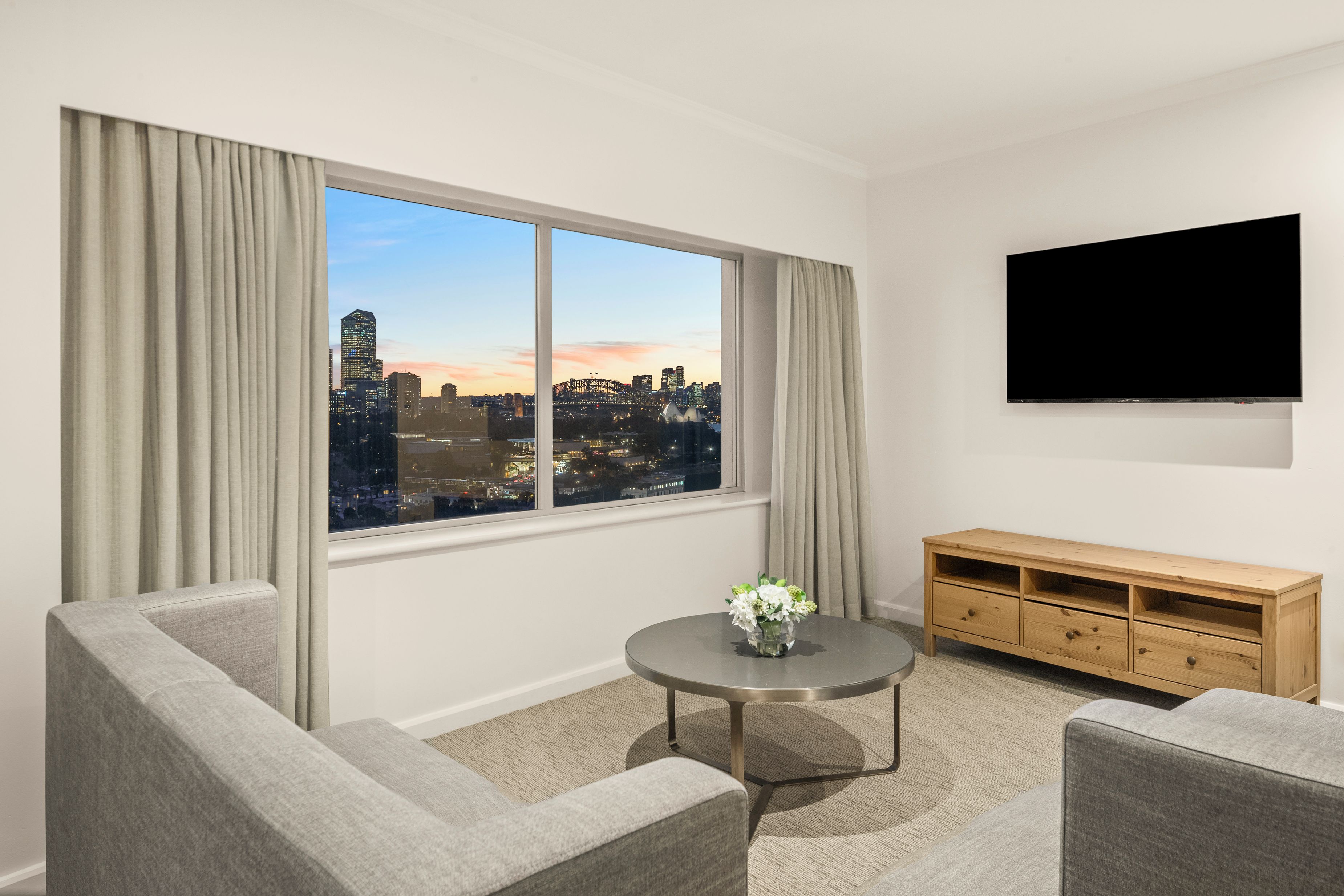 A modern living room with a large window, a flat-screen TV, and a wooden TV stand.