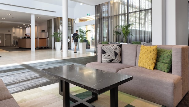A modern lobby with a sofa, a coffee table, and a reception desk. - Holiday Inn Sydney Potts Point by IHG (Potts Point)
