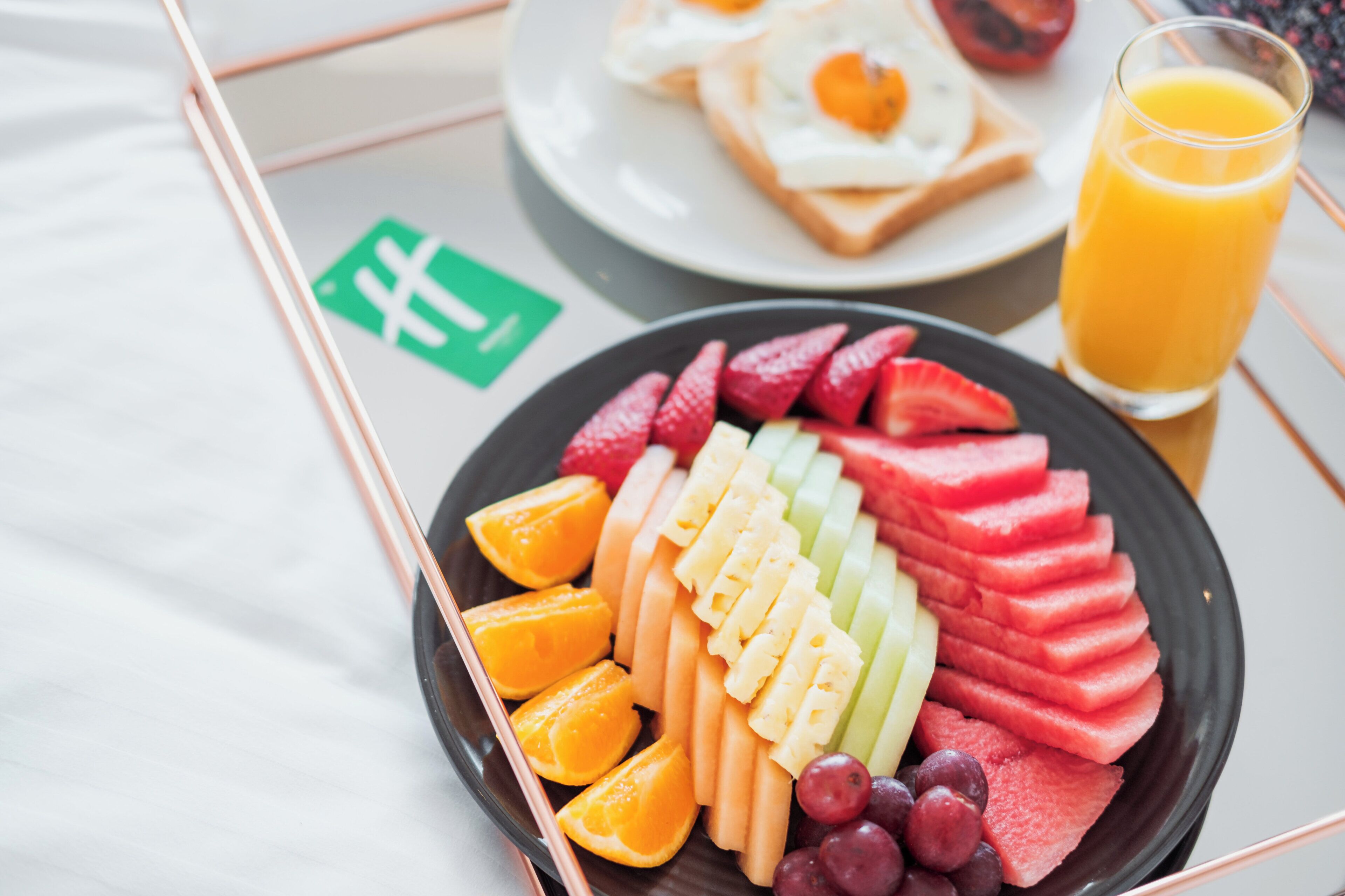 Een ontbijfwagen met gesneden fruit, toast met eieren en een glas sinaasappelsap.