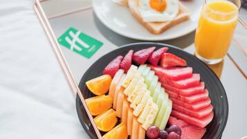 Een ontbijfwagen met gesneden fruit, toast met eieren en een glas sinaasappelsap.