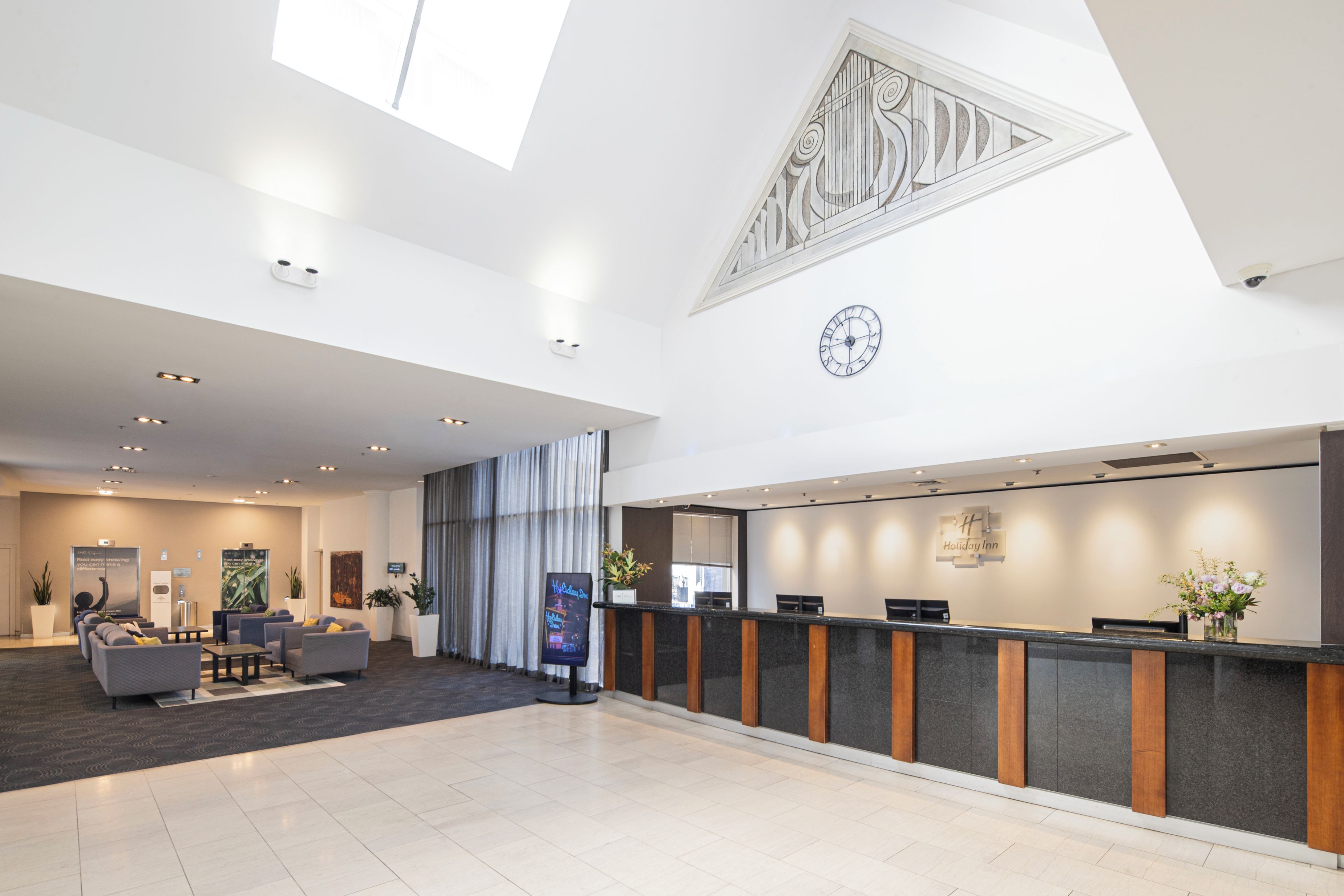 Een hotel receptie met een modern design, inclusief een receptiebalie, een zithoek en een grote klok aan de muur.