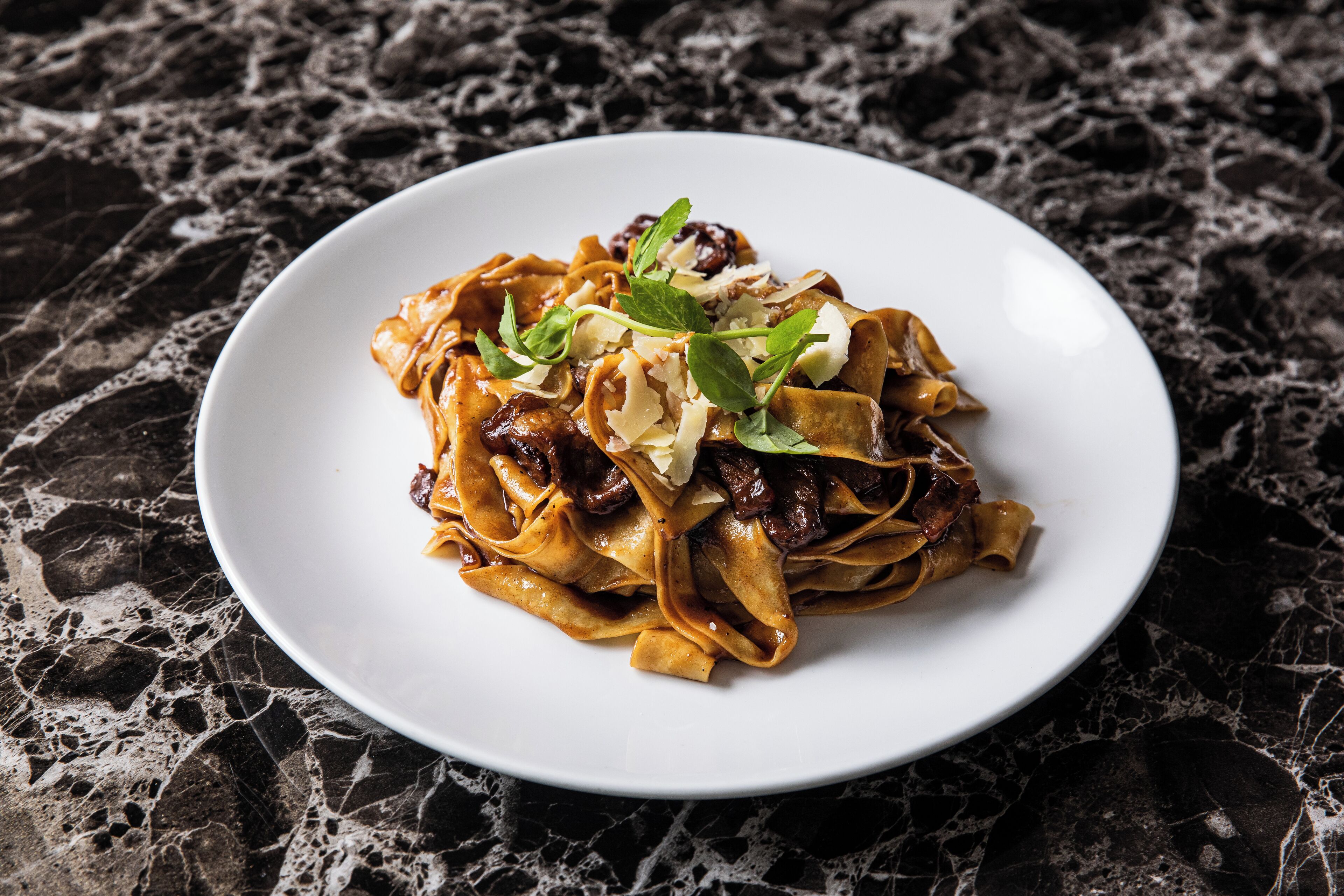 A plate of pasta with mushrooms and cheese on a marble surface.