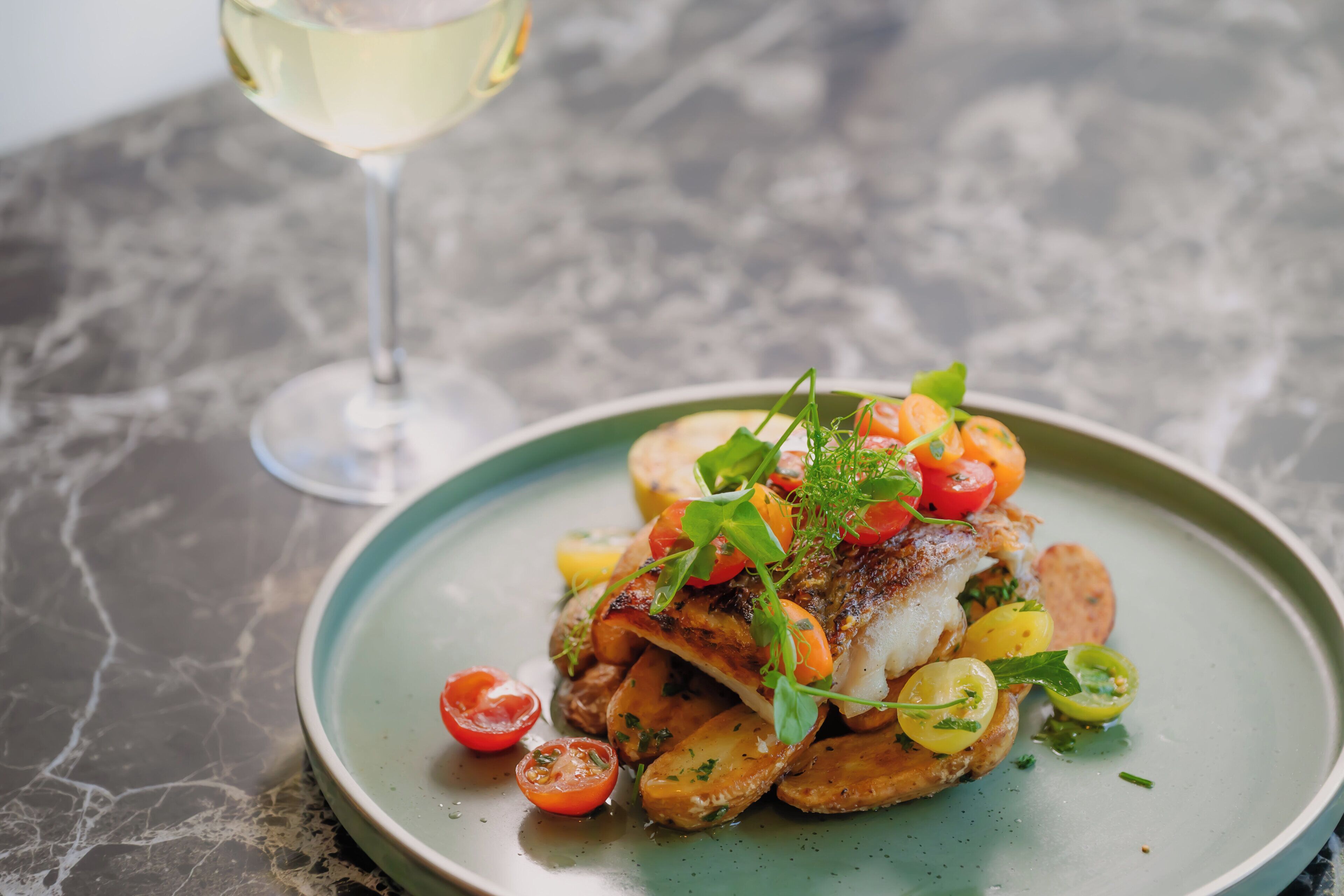 A plate of food with a glass of white wine on a marble table.