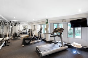 A gym with various exercise equipment, a first aid sign, and a TV on the wall.