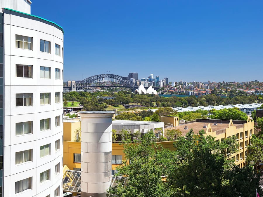Un edificio moderno con varios pisos y amplias ventanas, con vistas a un paisaje urbano que incluye un puente y una arquitectura distintiva.
