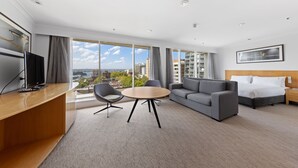 A modern hotel room with a large window, a sofa, a bed, a desk, and a television. - Holiday Inn Sydney Potts Point by IHG (Potts Point)
