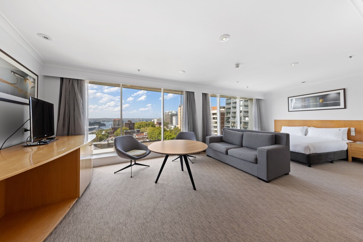 Et moderne hotelværelse med stort vindue, sofa, seng, skrivebord og fjernsyn.