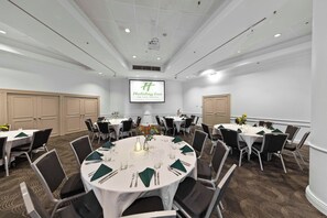 Ein Konferenzraum mit mehreren Tischen, gedeckt für ein Essen, ausgestattet mit Stühlen, Tischdecken und Besteck.