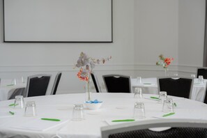 A conference room with tables set for meetings, each with a small vase of flowers, clear glassware, and green pens.