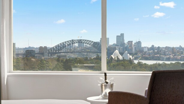 Ein Hotelzimmer mit großem Fenster und Blick auf das Opernhaus von Sydney sowie die Brücke von Sydney.