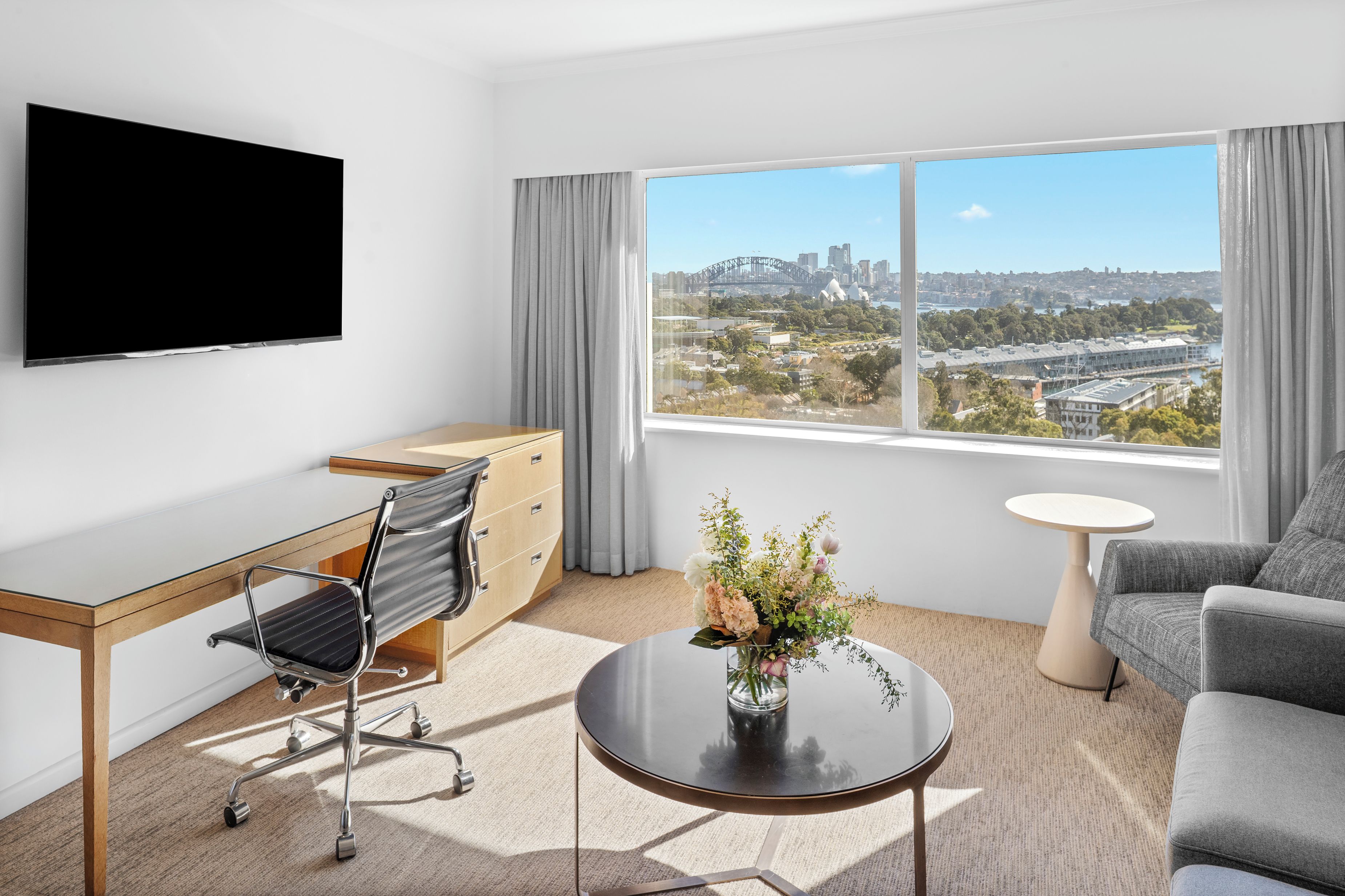 Une chambre d’hôtel moderne équipée d’un bureau, d’une chaise, d’un canapé et d’une grande fenêtre donnant sur la ville.