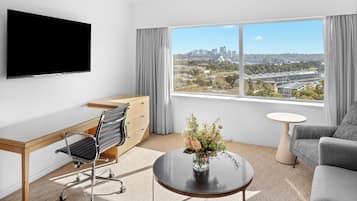 Une chambre d’hôtel moderne équipée d’un bureau, d’une chaise, d’un canapé et d’une grande fenêtre donnant sur la ville.