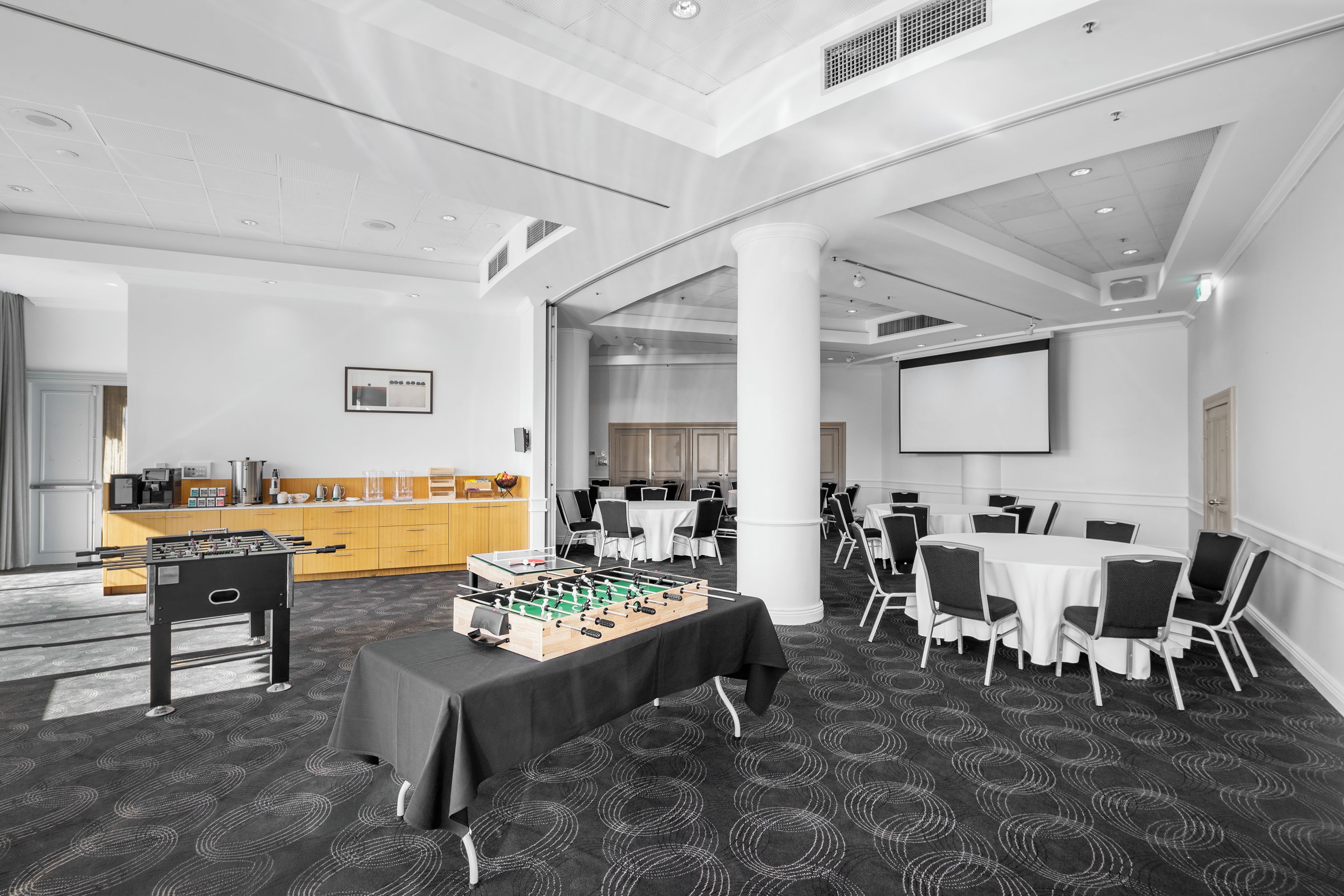 A conference room with a foosball table, white tables, and chairs, and a large screen.