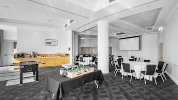 A conference room with a foosball table, white tables, and chairs, and a large screen.
