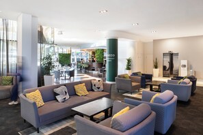 Un moderno vestíbulo de hotel con una zona de estar, un bar y un restaurante al fondo.