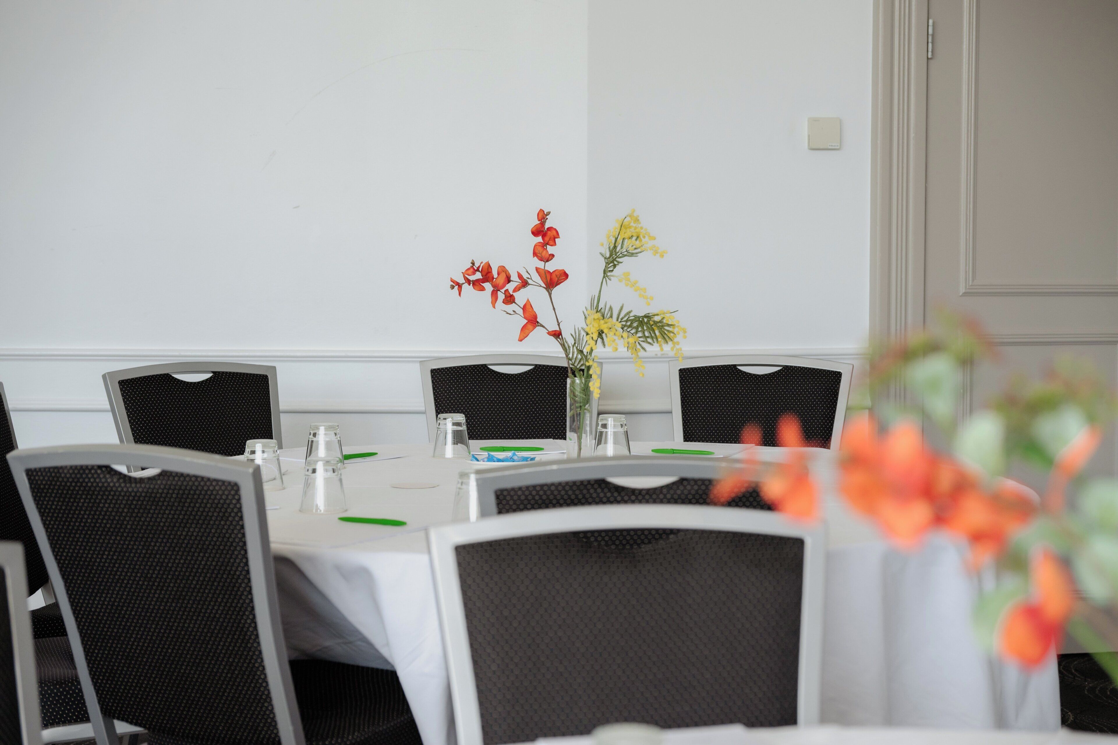 A conference room with a white table, black chairs, and a vase with flowers.