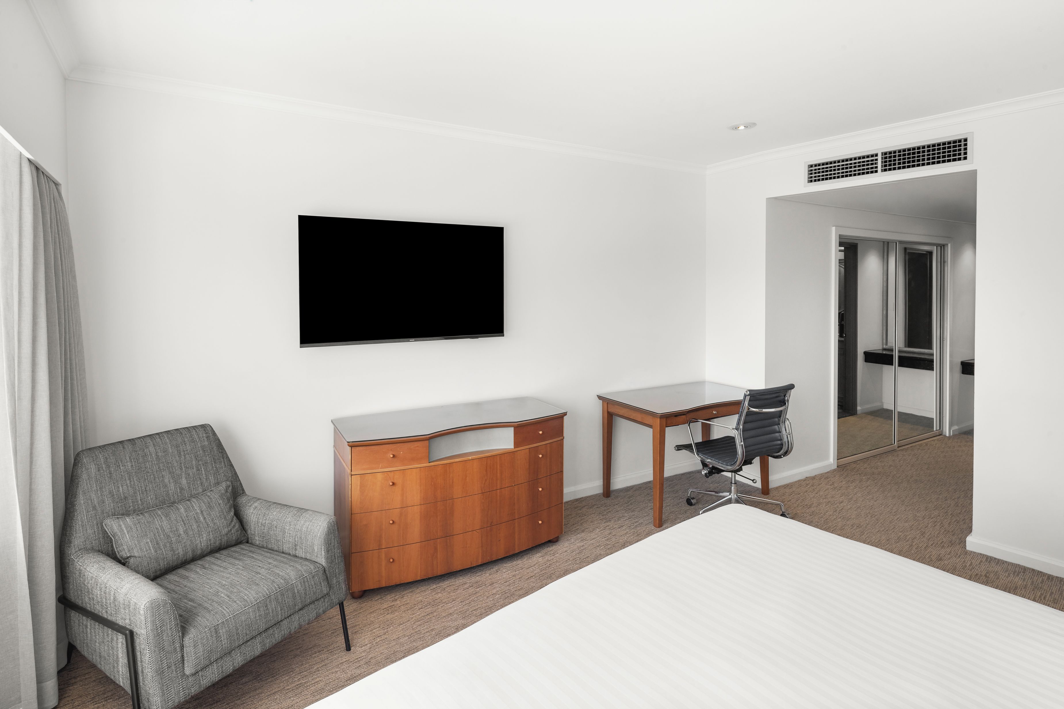 A hotel room with a bed, a desk, a chair, a TV, and a wardrobe.