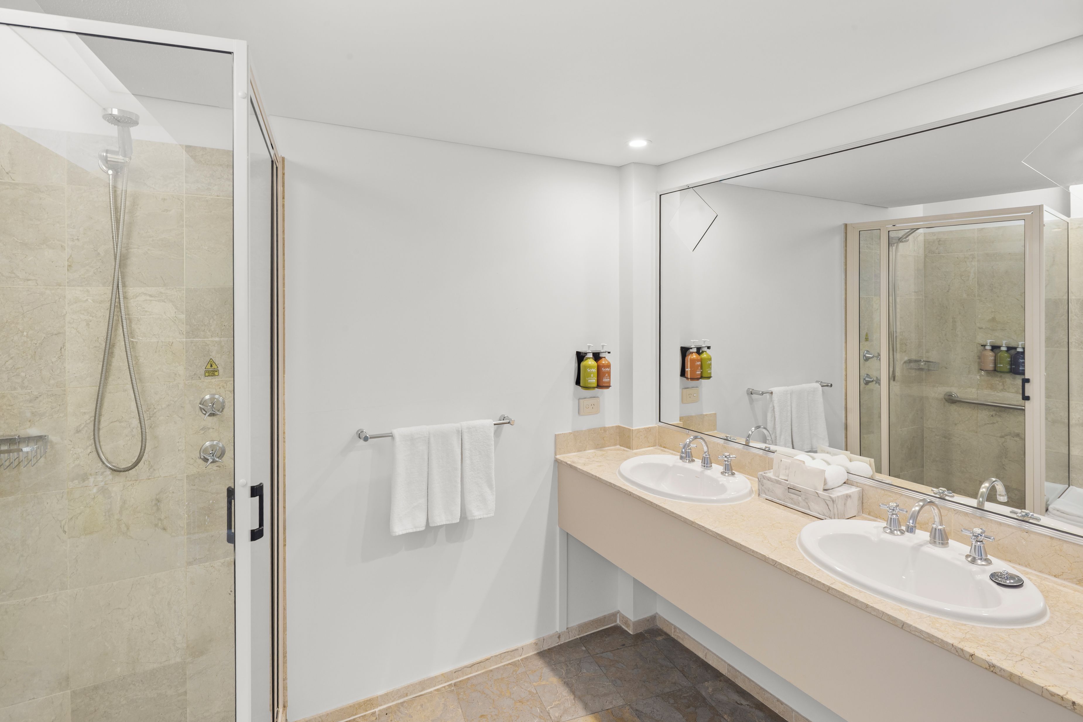 A modern bathroom with a glass-enclosed shower, two sinks, and a large mirror.