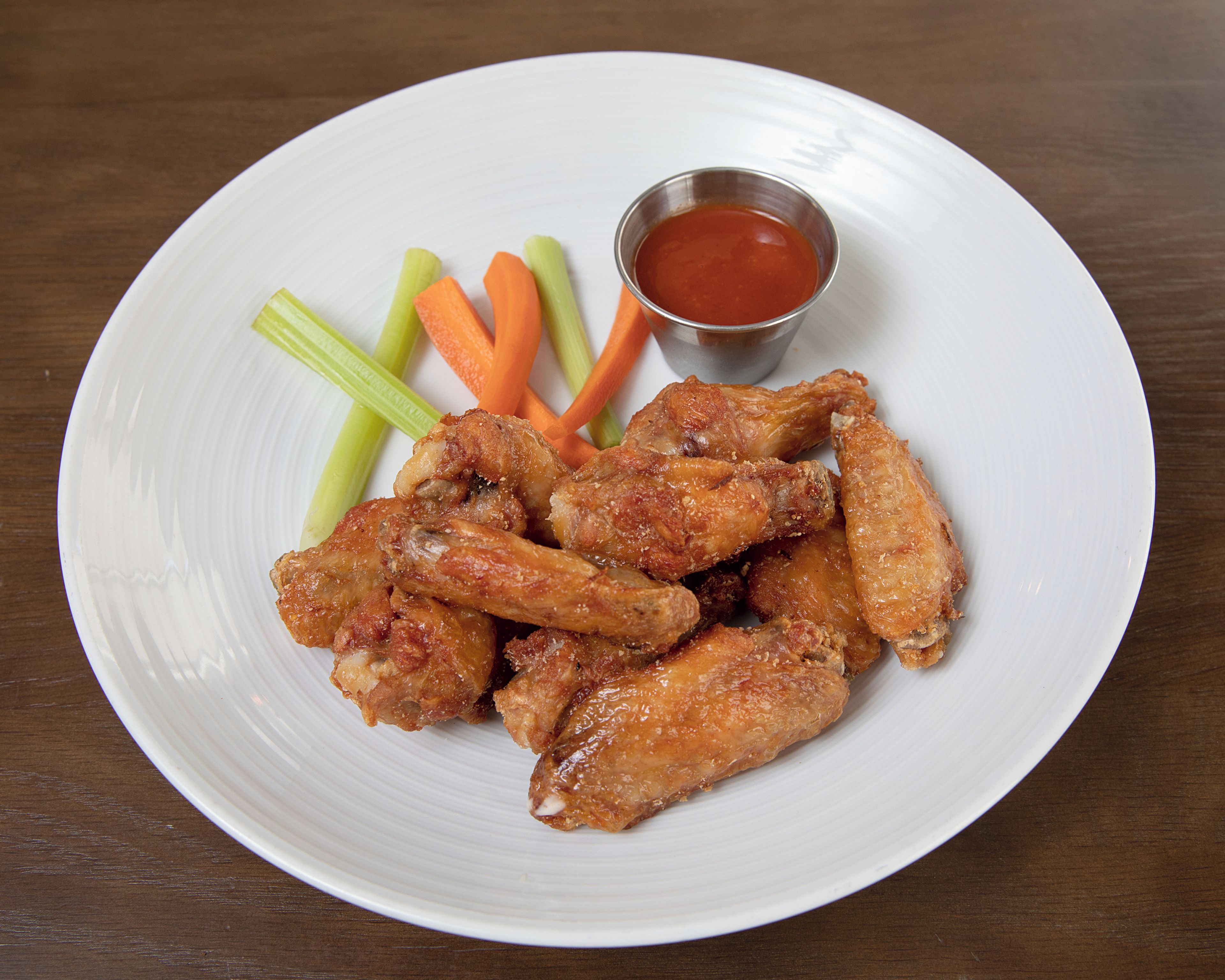A plate of chicken wings with celery and carrot sticks, and a small bowl of sauce.