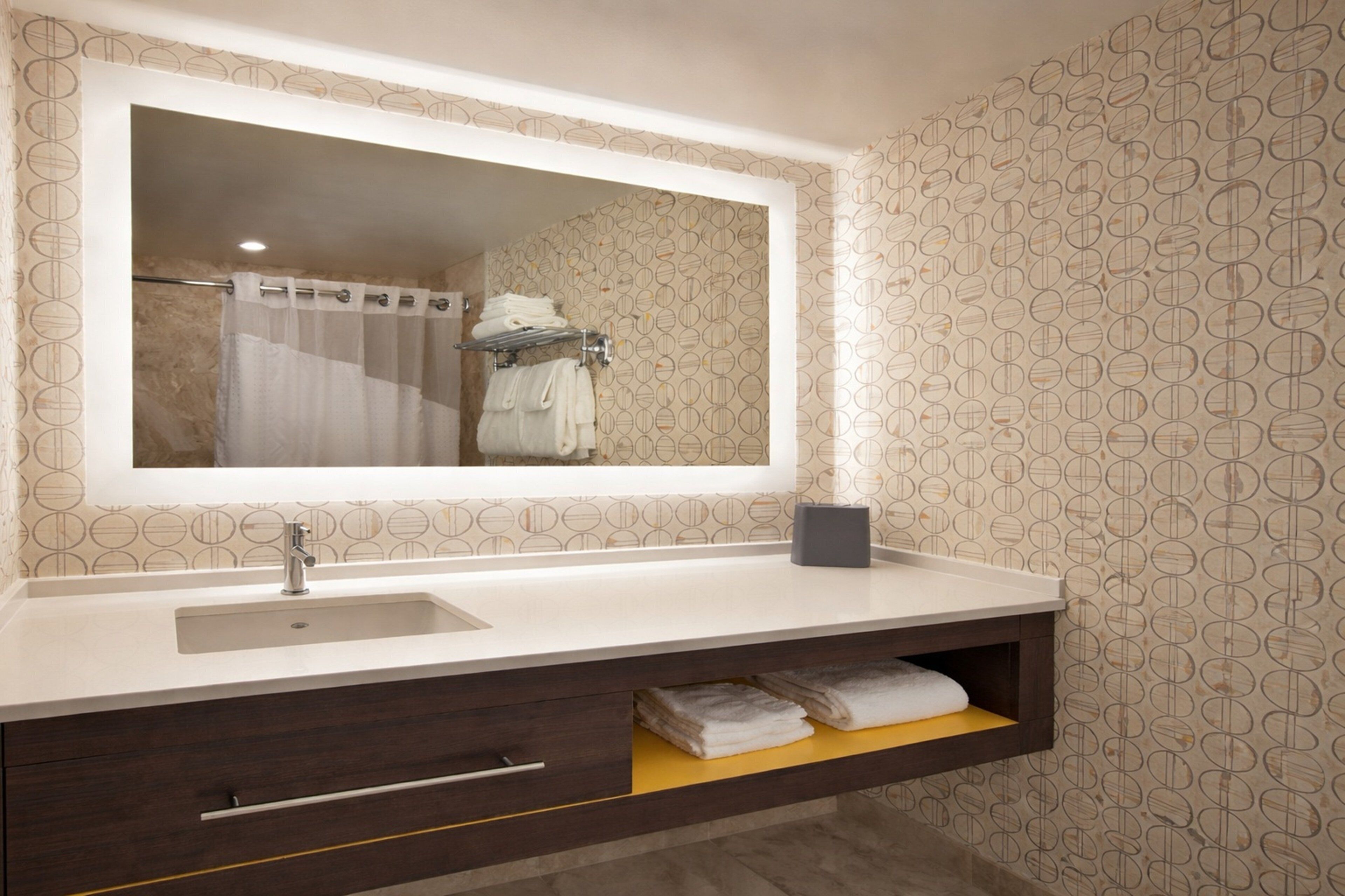 Une salle de bain avec un grand miroir, un lavabo, un porte-serviettes et une étagère avec des serviettes.