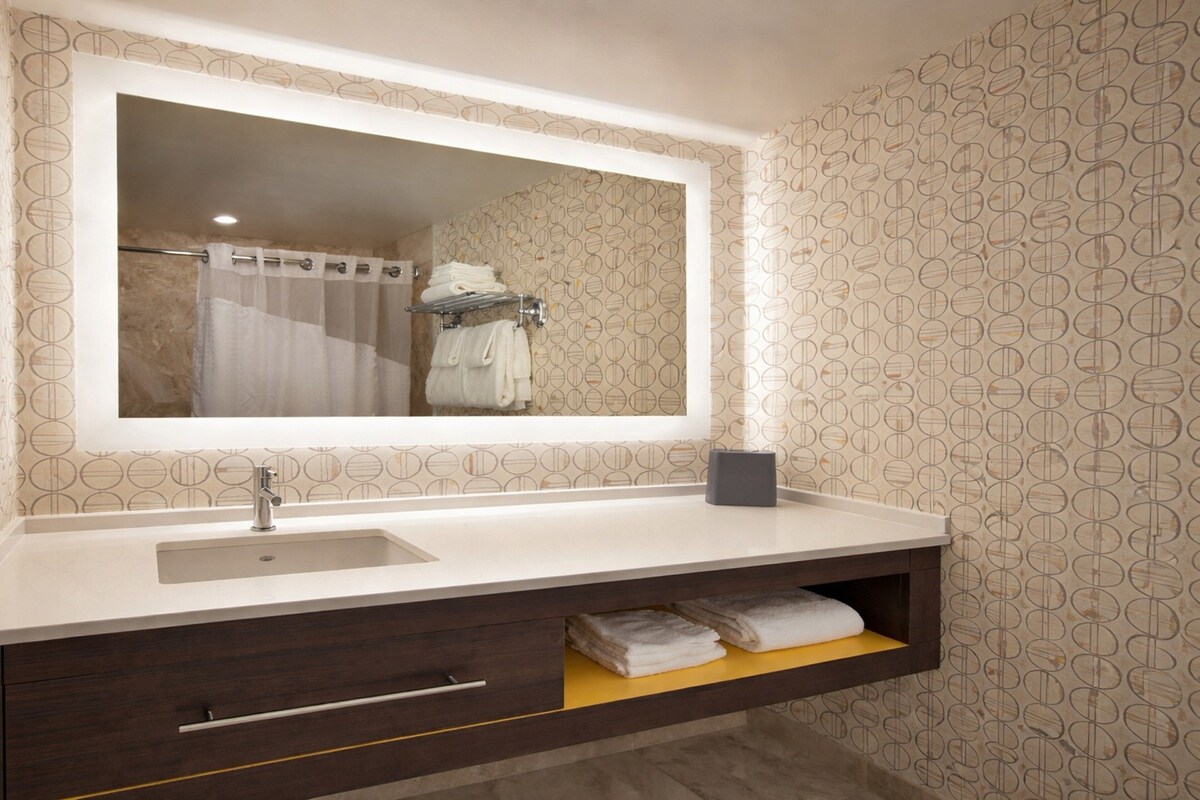 Une salle de bain avec un grand miroir, un lavabo, un porte-serviettes et une étagère avec des serviettes.