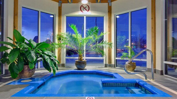 An indoor swimming pool with a view of the city at night, surrounded by large windows and potted plants. - Holiday Inn Montreal Longueuil by IHG (Longueuil)