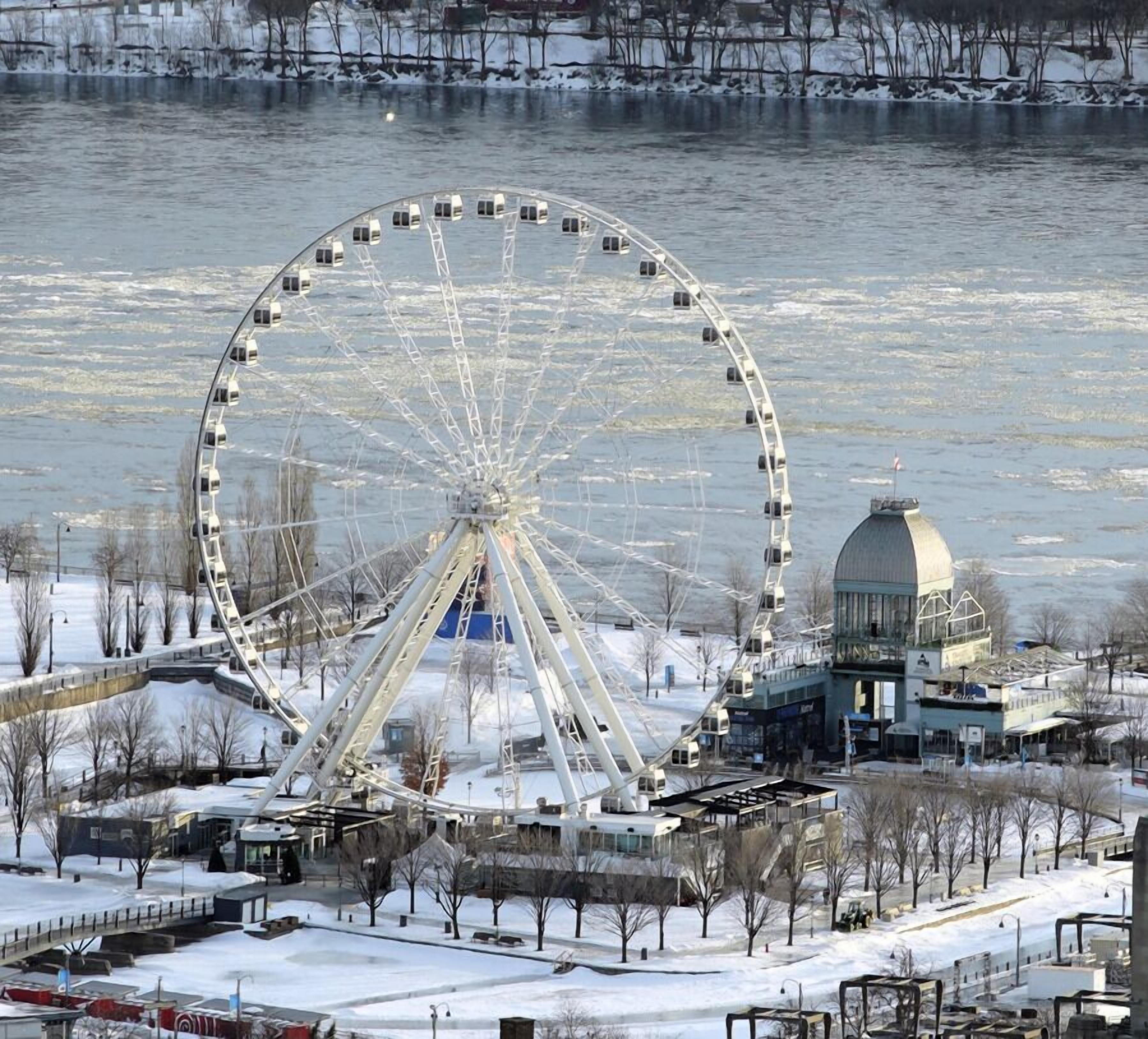 A large Ferris wheel with a viewing platform, surrounded by snow-covered ground and buildings.
