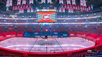 An indoor ice hockey arena with multiple tiers of seating, a central scoreboard, and banners hanging from the ceiling.