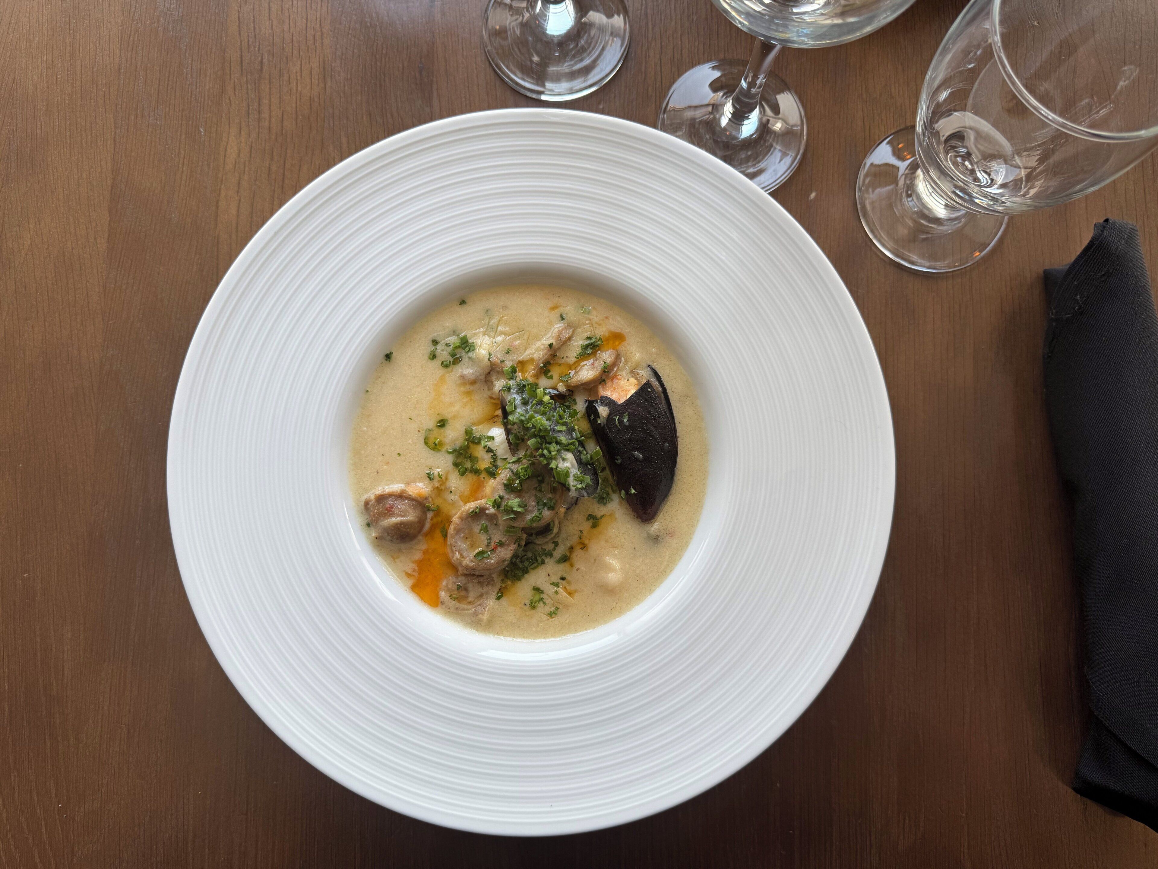 En hvid tallerken med cremet suppe, pyntet med krydderurter, på et træbord.